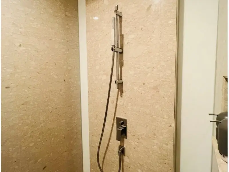 Detail shower modern dengan dinding marmer di kamar mandi apartemen 31 Sudirman Suites Makassar.