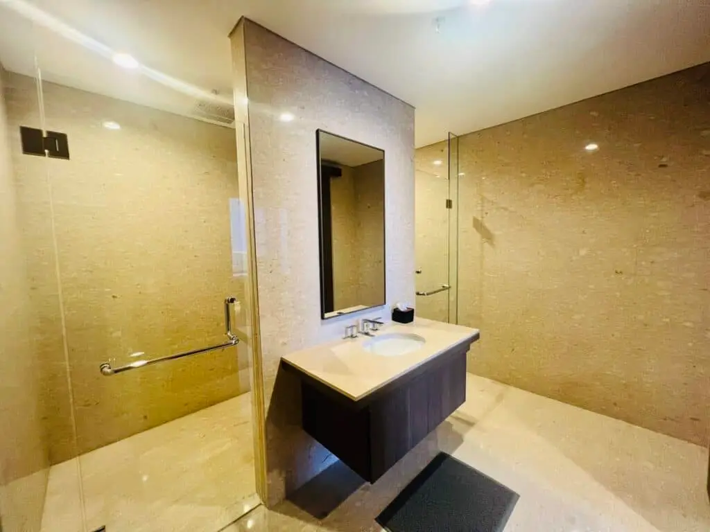Kamar mandi utama yang mewah dengan wastafel, cermin, dan area shower kaca di apartemen 31 Sudirman Suites Makassar.