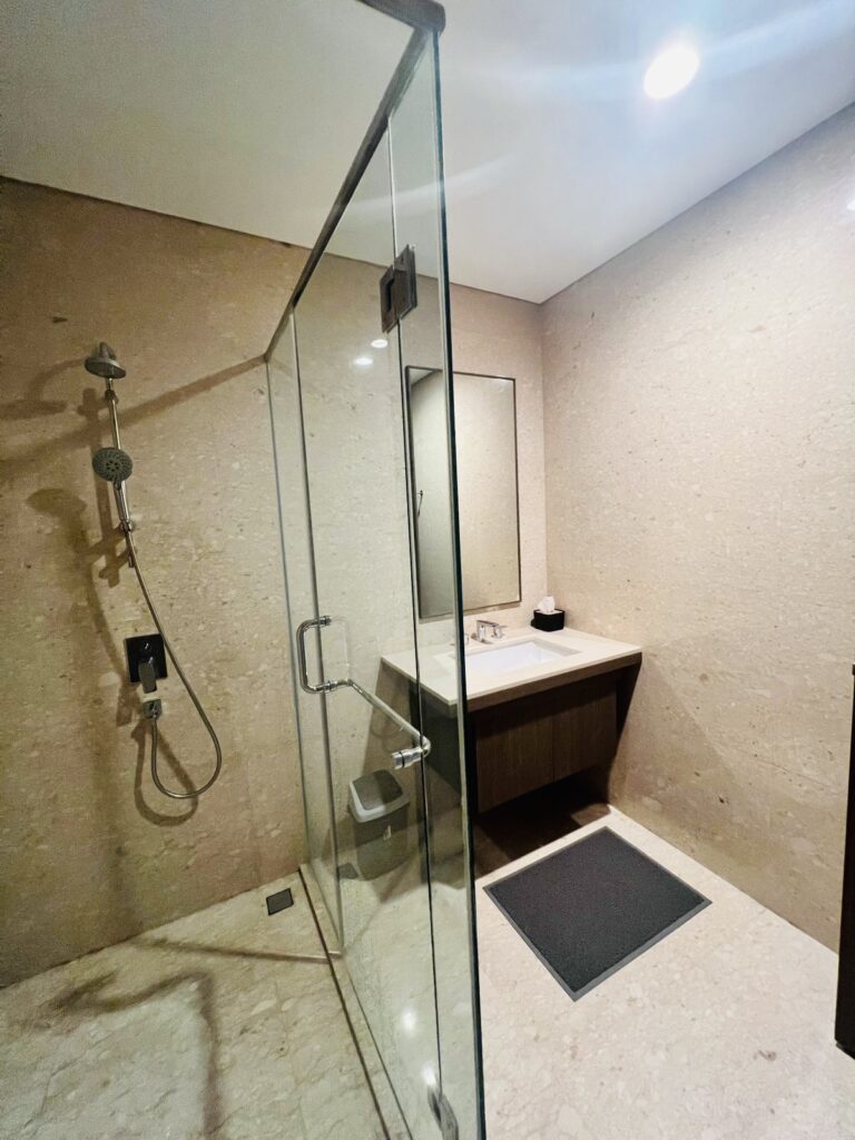 Bilik shower kaca dan area wastafel di kamar mandi apartemen 31 Sudirman Suites Makassar unit 3 kamar + 1 yang dijual.