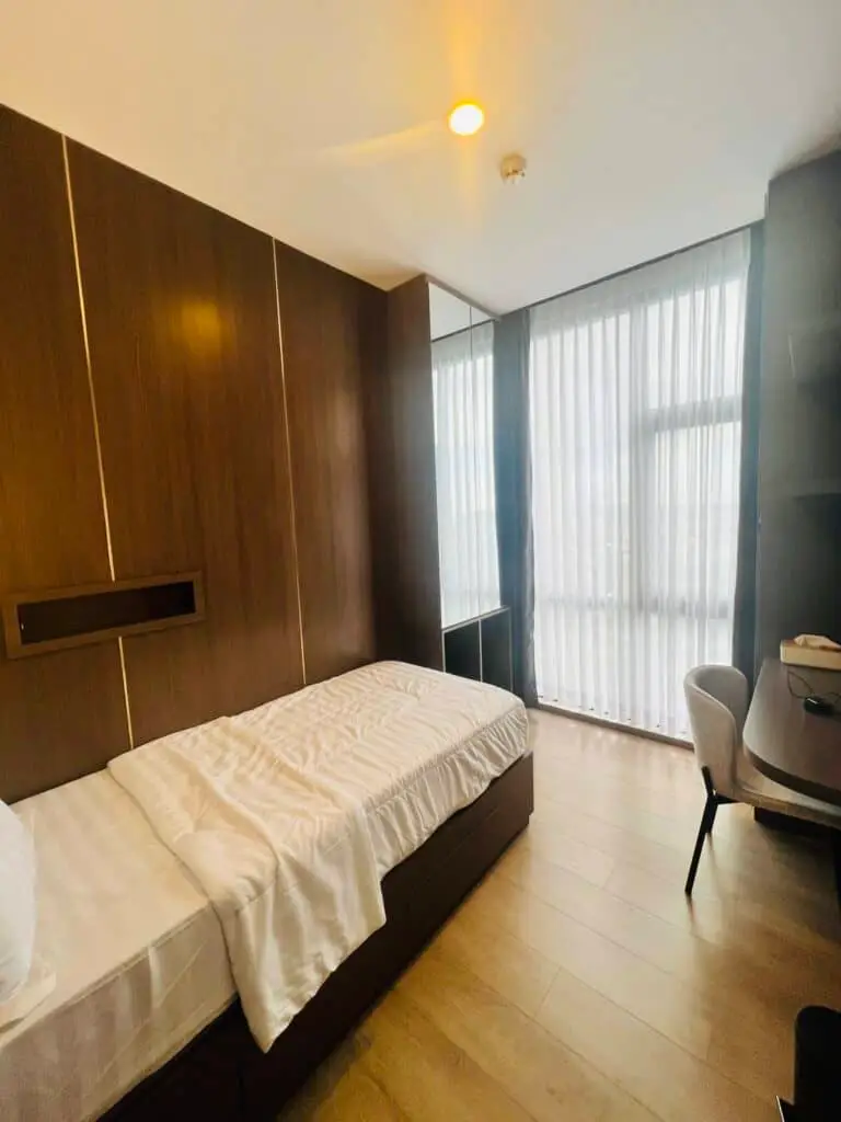 Interior kamar tidur dengan panel kayu, meja belajar, dan jendela besar yang memberikan pencahayaan alami di apartemen 31 Sudirman Suites Makassar.